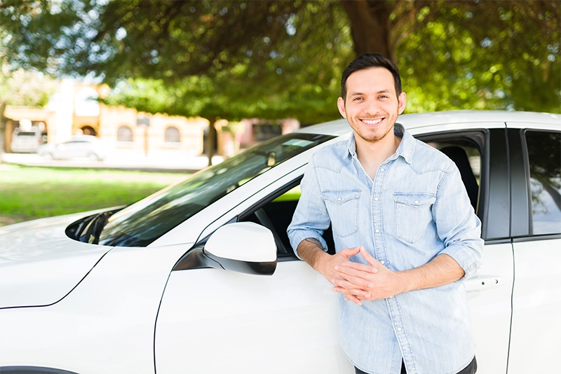 smiling young man standing near the driver side of a white car