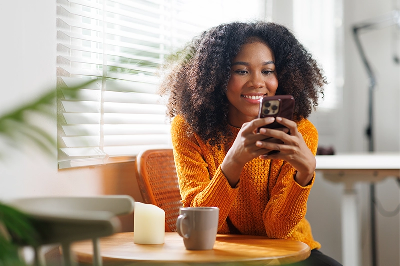 image of women sitting down at a table and smiling while she is looking at her mobile phone